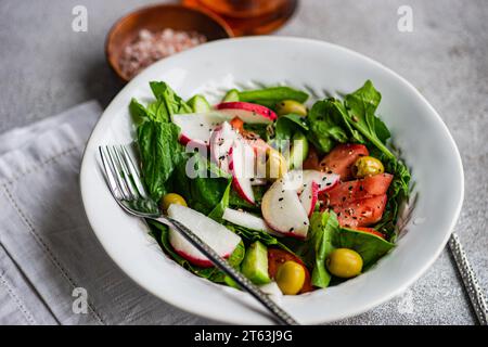 Salade de légumes fraîchement préparée avec des feuilles d'épinards biologiques, des tomates mûres, des radis croustillants et des olives vertes magnifiquement présentés dans un bo blanc Banque D'Images