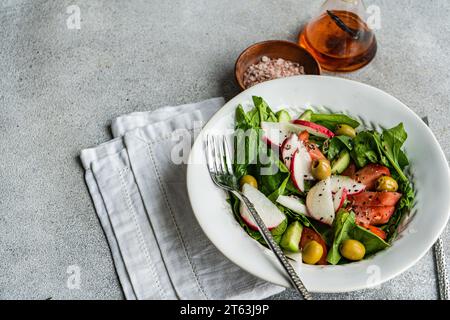 Salade de légumes fraîchement préparée avec des feuilles d'épinards biologiques, des tomates mûres, des radis croustillants et des olives vertes magnifiquement présentés dans un bo blanc Banque D'Images