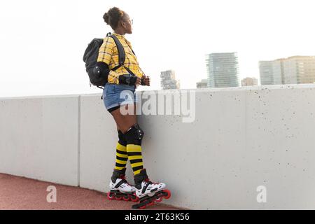 Pensive jeune femme afro-américaine en patins à roulettes portant sac à dos tout en se tenant au skate Park Banque D'Images