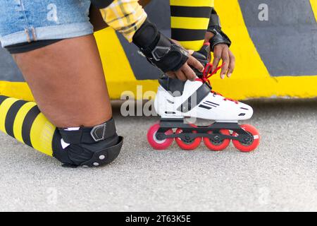 Section basse d'une jeune femme afro-américaine portant une chaussure de patin à roulettes tout en agenouillant au skate Park Banque D'Images