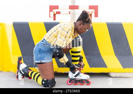 Corps entier de jeune femme afro-américaine portant la chaussure de patin à roulettes tout en agenouillant par barricade au skate Park Banque D'Images