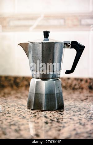 Un pot de moka vintage argenté se dresse sur un comptoir de granit éclairé par une lumière naturelle douce Banque D'Images