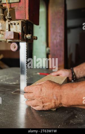 Gros plan des mains d'un vieux menuisier anonyme guidant une planche de bois à travers une scie verticale dans un atelier de Toledo Banque D'Images