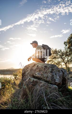 Vue latérale d'un randonneur masculin s'accroupant sur un rocher tout en contemplant des vues pendant le coucher du soleil à Pantano de Layos, Tolède, Espagne Banque D'Images