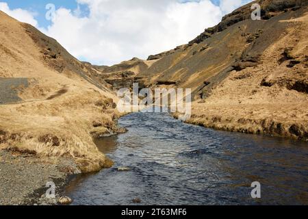 Vue tranquille du ruisseau serein coulant entre les montagnes rocheuses rugueuses contre le ciel nuageux en Islande Banque D'Images