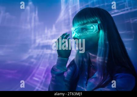 Vue latérale de la jeune femme hypnotisée par des lunettes LED VR modernes et immergée dans l'expérience de réalité virtuelle sur des lumières de projecteur éclairées Banque D'Images
