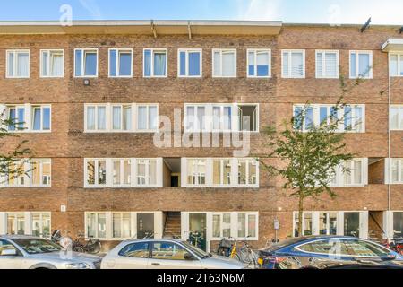 Voitures et vélos garés en face de l'immeuble d'appartements avec des fenêtres et des murs de briques dans la ville pendant la journée ensoleillée Banque D'Images