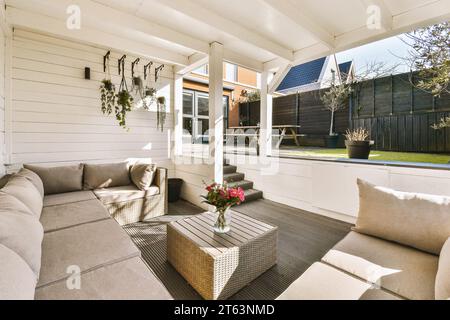 Canapé gris confortable avec vase de fleur sur la table basse disposé dans le porche blanc en face de la cour arrière avec clôture à la journée Banque D'Images