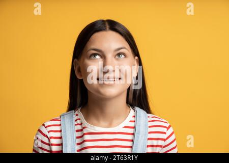 Bannière publicitaire fille brune souriante regardant vers le haut sur l'espace de copie isolé sur fond jaune. Banque D'Images