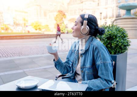 femme en denim et casque buvant du café et écoutant de la musique ou des livres audio dans le café. Concept de style de vie Banque D'Images