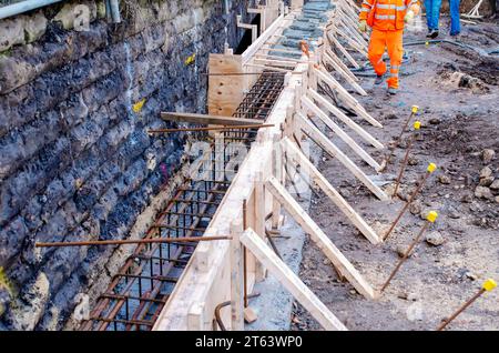 Les constructeurs versent du béton prêt à l'emploi humide dans le coffrage le long de la semelle d'un vieux pont pour créer un support supplémentaire pour celui-ci Banque D'Images