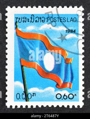 Timbre postal annulé imprimé par le Laos, qui montre le drapeau national du Laos, célébrant la fête nationale, vers 1984. Banque D'Images