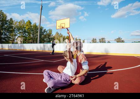 Objectif. Une femme émotionnelle et une adolescente encouragent leur frère, leur fils ou leur ami, un petit garçon lance un ballon de basket-ball et un ballon Banque D'Images