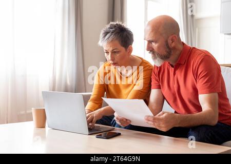 Portrait de conjoints matures sérieux avec ordinateur portable faisant du paperwork ensemble Banque D'Images