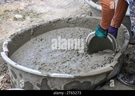 Un travailleur utilise un godet pour ramasser du béton prêt à l'emploi dans des travaux de construction sur site. Banque D'Images