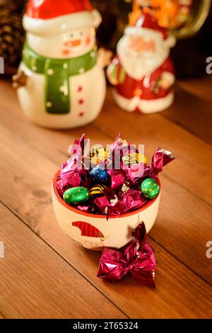 Nature morte de Noël avec des figures en porcelaine et d'autres objets, des bonbons et des chocolats, sur une table en bois avec un fond sombre. Banque D'Images