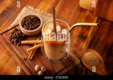 Café glacé servi dans une tasse en verre à double paroi et paille de métal, une boisson fraîche d'été préparée avec des glaçons et des épices, cannelle, muscade, vanille, mu Banque D'Images