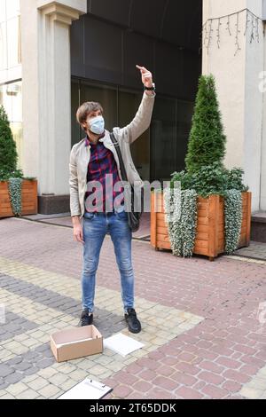 Un homme portant un masque de protection, qui a perdu son emploi en raison de la crise économique pendant la pandémie, se met en grève dans la rue devant un bureau Banque D'Images