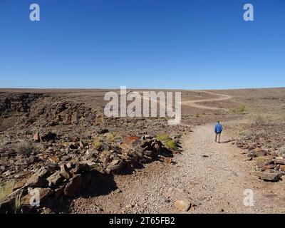 Un homme marchant sur un chemin près de Fish River Canyon, Namibie, avec des paysages arides et un ciel parfaitement bleu. Banque D'Images