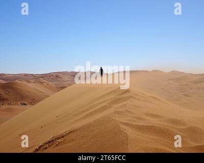 Un homme marchant jusqu'à une dune de sable près de Deadvlei, dans le parc national Namib-Naukluft près de Sesriem, Namibie Banque D'Images