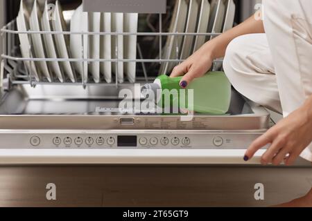 la main féminine verse le liquide de rinçage dans le compartiment lave-vaisselle de la cuisine blanche moderne Banque D'Images