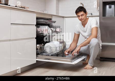 bel homme mettant la tablette de détergent dans le lave-vaisselle dans la cuisine Banque D'Images