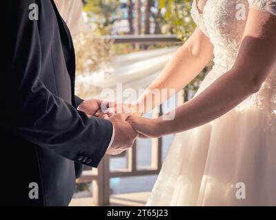 Gros plan du marié et de la mariée en costume noir tenant les mains de la mariée le jour de la cérémonie de mariage. Banque D'Images
