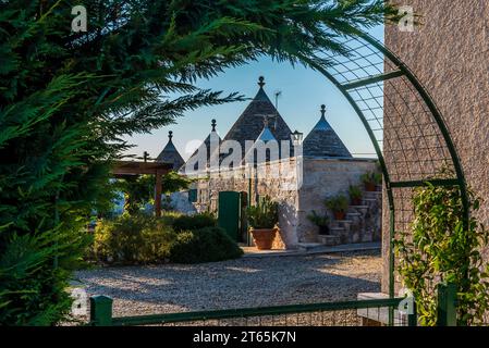 Maisons traditionnelles Trulli encadrées par une arche à feuilles persistantes près de Martina Franca, Bari, Italie en été. Banque D'Images