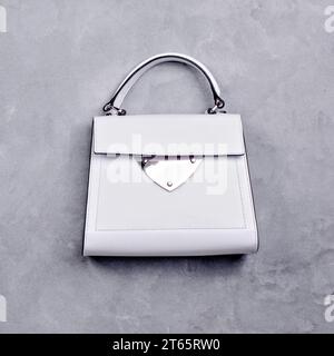 Élégant sac à main pour femme en cuir blanc avec une poignée supérieure, une garniture noire, un accent en métal argenté et des pieds isolés sur un fond gris. Créativité minimale Banque D'Images