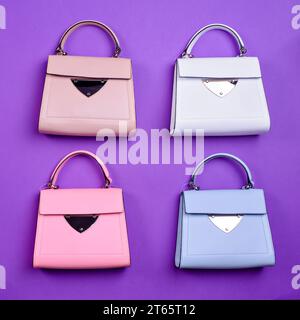 Pose à plat de quatre sacs à poignée supérieure en cuir tendance pour femmes du même design mais de couleurs différentes sur un fond violet. Blog ou magazine de mode. Choo Banque D'Images