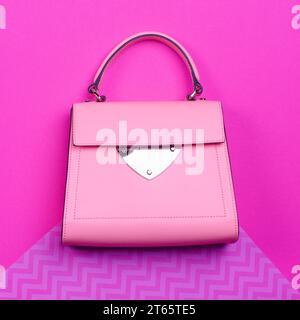 Un sac contemporain féminin à poignée supérieure en cuir rose avec bordure noire, un accent en métal et des pieds isolés contre un dos coloré à motifs en zigzag Banque D'Images