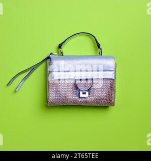 Sac à main féminin de conception tissée audacieuse avec rabat en cuir argenté, poignée supérieure et tirette à glissière isolé sur un fond vert avec espace de copie. Design créatif Banque D'Images