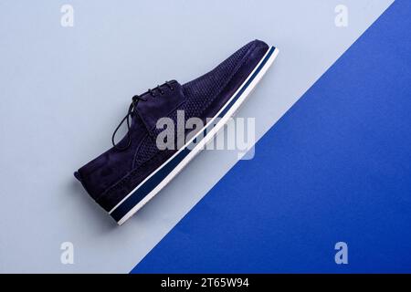 Vue latérale de la chaussure moderne décontractée en daim perforé bleu foncé avec semelle blanche et bleue isolée sur un fond géométrique créatif avec espace copie. Banque D'Images