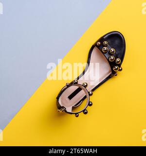 Sandale à la mode en cuir noir à lanière pour femmes avec semelle intérieure beige, décorée de grandes perles dorées sur un fond bleu-jaune créatif avec copie Banque D'Images