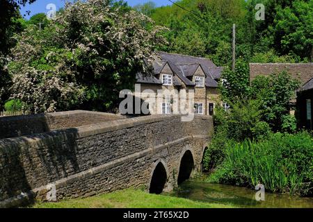Ford : Old Bridge over By Brook avec White Hart pub et fleurs au village Ford près de Castle Combe, Cotswolds, Wiltshire, Angleterre, Royaume-Uni Banque D'Images