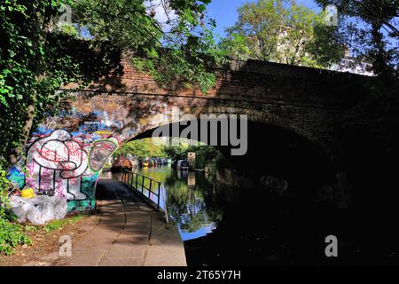 Pont en brique voûté sur Regents Canal à Regents Park Road avec graffitis colorés, bateaux de canal et reflets à Camden Town, Londres, Angleterre Banque D'Images