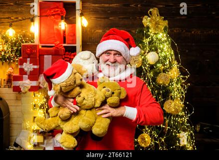 Vacances de Noël. Père Noël souriant avec de nombreux ours en peluche. Homme barbu dans le chapeau du Père Noël avec des ours en peluche dans la chambre décorée pour Noël. Père Noël Banque D'Images