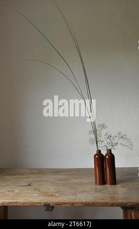 Composition artistique minimaliste. Fragments d'une ancienne maison de campagne à l'intérieur - murs éclairés plâtrés, une ancienne table en bois, bouteilles vitrées en argile Banque D'Images