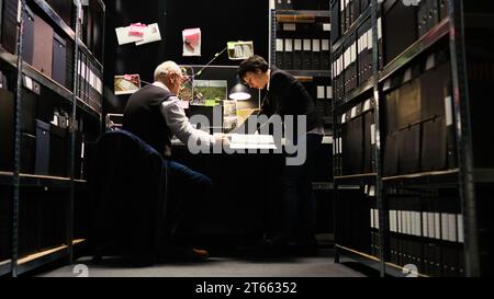 L'équipe d'experts lit les dossiers de cas dans la salle d'incident de la police, en utilisant des documents et des dossiers confidentiels. Les agents chargés de l'application de la loi vérifient l'authenticité des preuves, découvrent des indices. Prise de vue sur trépied. Banque D'Images