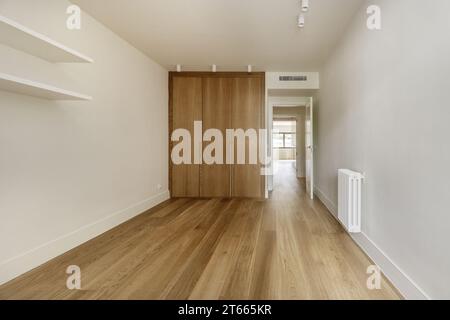 Couloir d'accès à une chambre avec armoires encastrées avec portes en chêne clair sur mesure, murs peints en blanc, étagères blanches sur le mur, spots blancs Banque D'Images