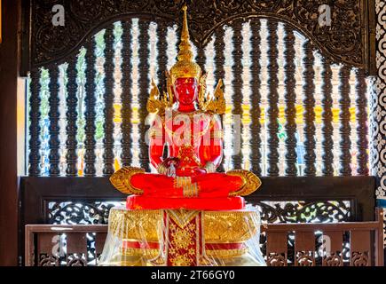 La lumière du soleil brille à travers l'image transparente de Bouddha, à l'intérieur du temple, belle, vibrante, ornée rouge et dorée, debout devant une fenêtre voisine Banque D'Images