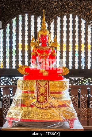 La lumière du soleil brille à travers l'image transparente de Bouddha, à l'intérieur du temple, belle, vibrante, ornée rouge et dorée, debout devant une fenêtre voisine Banque D'Images