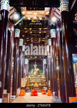 Illuminé par des lumières à l'intérieur de l'ancienne structure, les moines chantent et prient devant le Bouddha d'or, des décorations exquises et complexes et des sculptures ornent th Banque D'Images