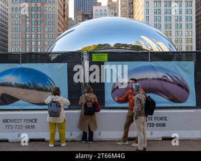 Les touristes essaient de voir Cloud Gate aka The Bean à travers une clôture de construction. Le plaza est fermé pour rénovation jusqu'au printemps 2024. Chicago, Illinois. Banque D'Images