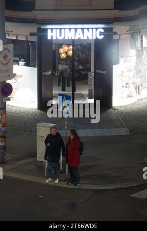 Un couple d'hommes et de femmes se promènent devant le magasin Humanic, Vienne Autriche la nuit en hiver, photographiés depuis un grand bâtiment Banque D'Images