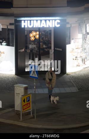 Une femme et son chien marchent devant le magasin Humanic, Vienne Autriche la nuit en hiver, photographiés depuis un grand bâtiment Banque D'Images