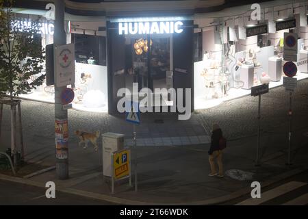 Un homme et son chien marchent devant le magasin Humanic, Vienne Autriche la nuit en hiver, photographiés depuis un grand bâtiment Banque D'Images