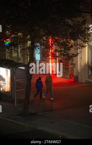 Deux personnes en vêtements d'hiver marchant sur le trottoir sur fond de lumières rouges de la ville la nuit en hiver, Vienne Autriche Banque D'Images