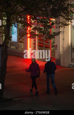 Deux personnes en vêtements d'hiver marchant sur le trottoir sur fond de lumières rouges de la ville la nuit en hiver, Vienne Autriche Banque D'Images