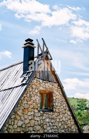 Toit triangulaire d'une maison en pierre avec escalier et cheminée contre un ciel nuageux Banque D'Images